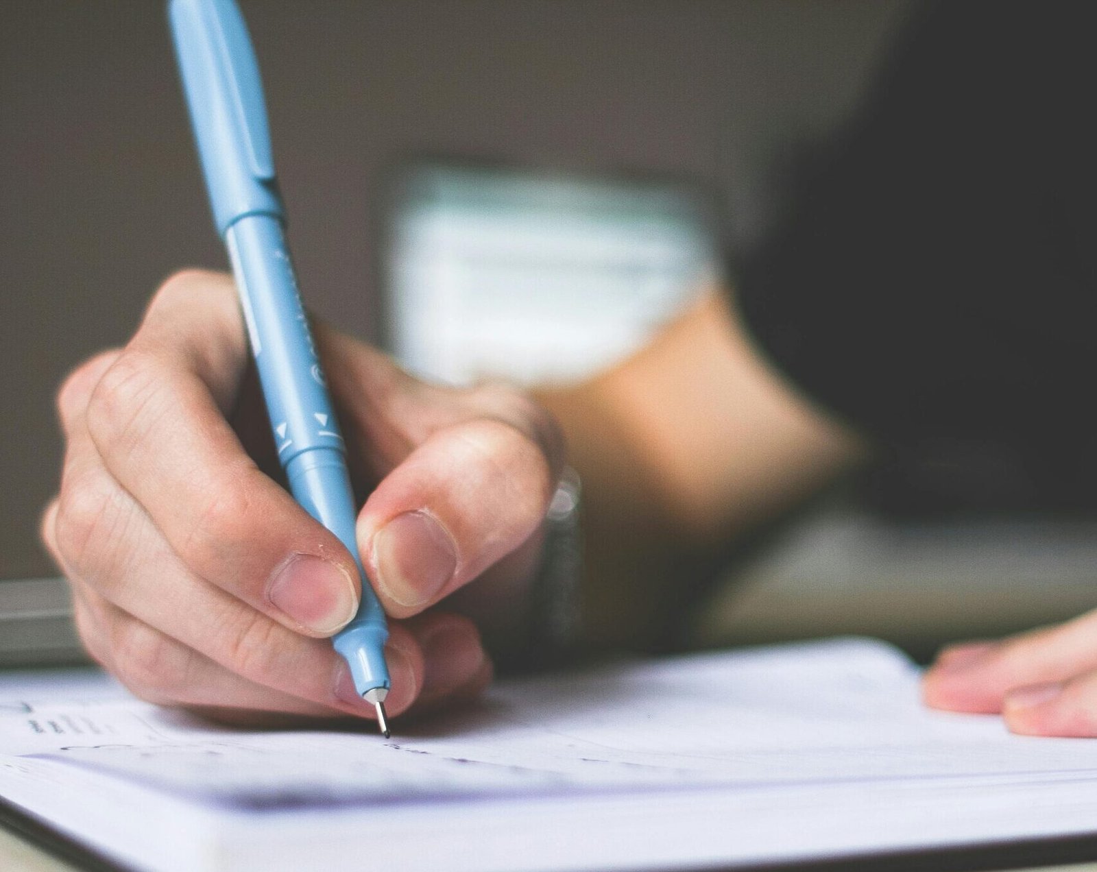 Close-up of hand writing in notebook using a blue pen, focus on creativity.